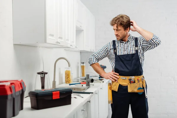 Selective focus of thoughtful plumber looking at kitchen sink near tools and toolboxes on kitchen worktop — Stock Photo