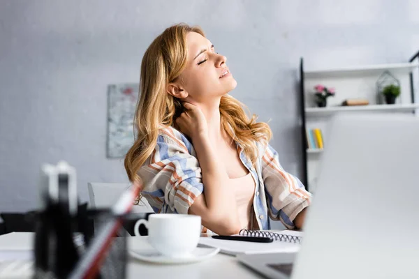 Selective focus of exhausted woman touching neck while working at table — Stock Photo