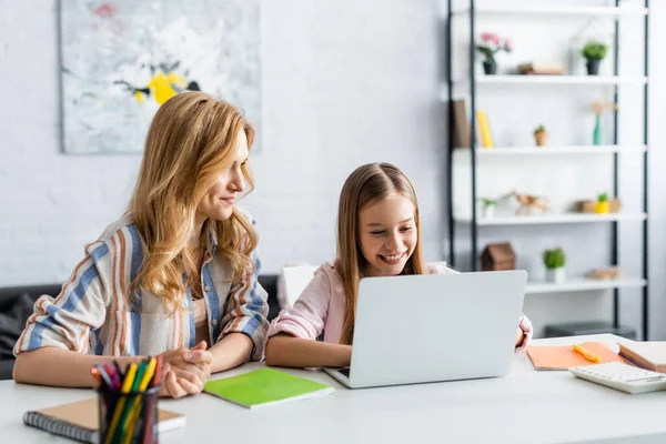 Selective focus of smiling kid using laptop near mother during online education — Stock Photo