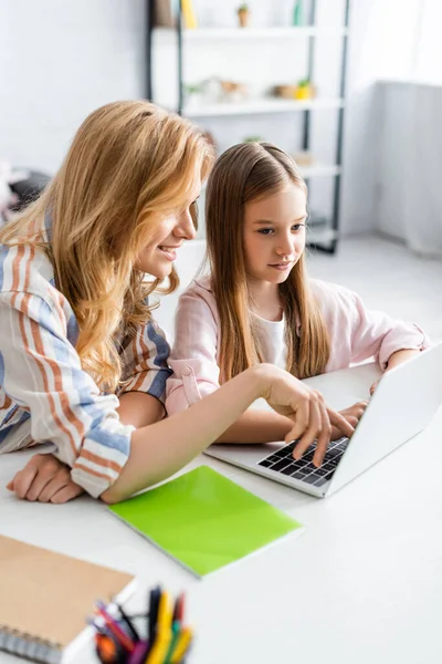 Concentration sélective de la mère souriante utilisant un ordinateur portable près de sa fille pendant le webinaire à la maison — Photo de stock