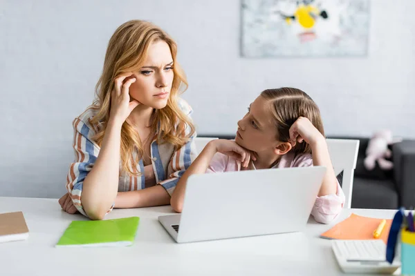 Selective focus of kid looking at thoughtful mother near laptop at home — Stock Photo