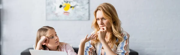 Panoramic shot of kid pointing with hand near pensive mother and laptop at home — Stock Photo