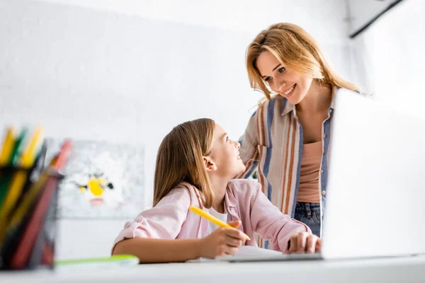 Селективное внимание улыбающегося ребенка, смотрящего на мать во время онлайн-обучения дома — стоковое фото
