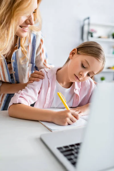 Enfoque selectivo de la mujer sonriente mirando a los niños escribir en el portátil cerca de la computadora portátil - foto de stock