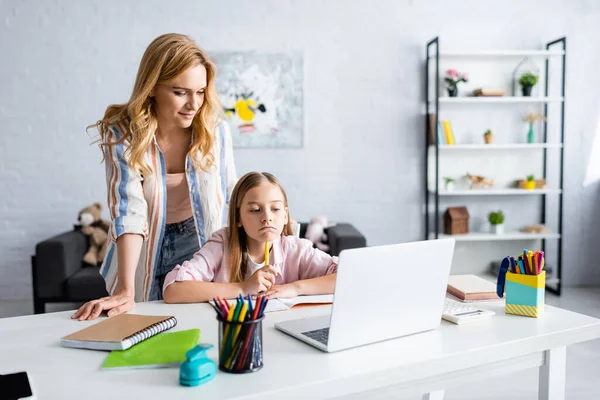 Selective focus of mother standing near thoughtful daughter during online education — Stock Photo