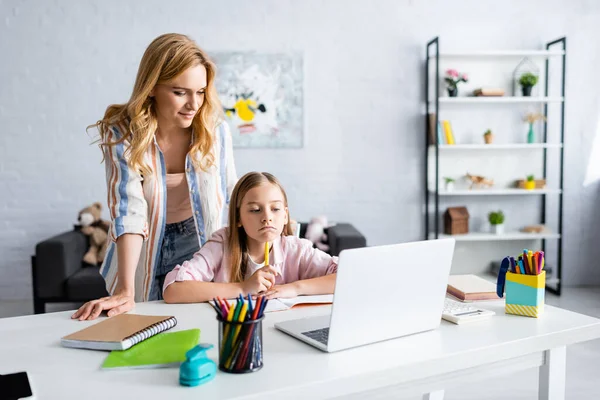 Selektiver Fokus der Mutter, die während der Online-Ausbildung neben der nachdenklichen Tochter steht — Stockfoto