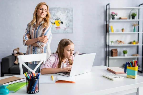 Foco seletivo da mulher olhando para a filha usando laptop perto de artigos de papelaria na mesa — Fotografia de Stock