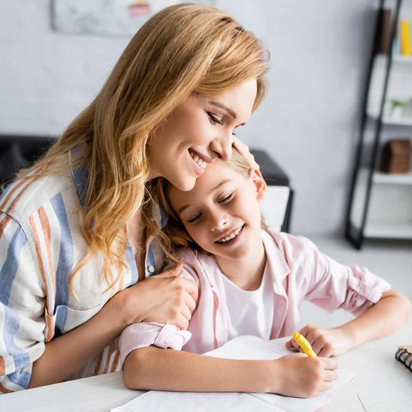 Smiling mother embracing kid writing on notebook at table — Stock Photo