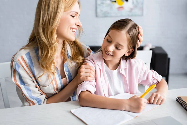 Smiling woman embracing child holding pen near notebooks on table — Stock Photo