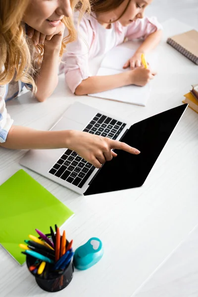 Високий кут зору жінки вказує пальцем на ноутбук, коли дочка пише на ноутбуці за столом — стокове фото