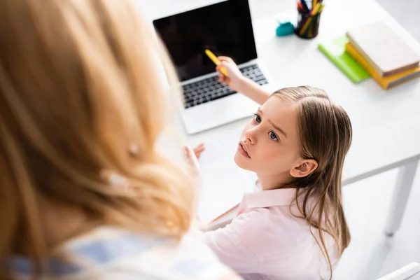Vista aérea del niño mirando a la madre mientras apunta a la computadora portátil durante la educación en línea - foto de stock