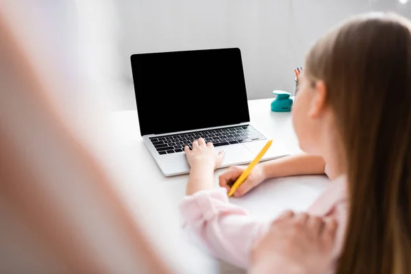 Selective focus of mother standing near daughter using laptop and writing on notebook — Stock Photo