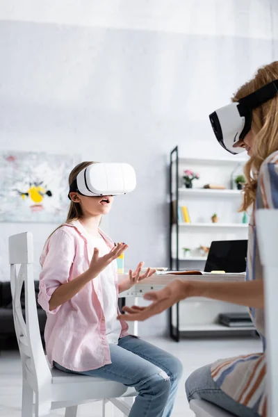 Selective focus of excited child in virtual reality headset sitting near mother and stationery on table — Stock Photo