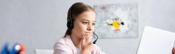 Panoramic crop of pensive kid in headset looking at laptop — Stock Photo