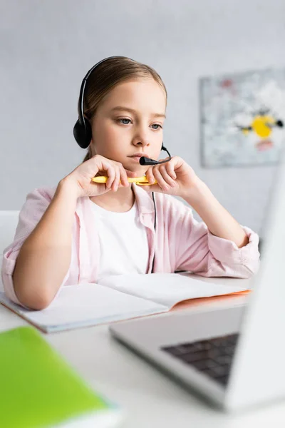 Enfoque selectivo del niño en lápiz de sujeción de auriculares y mirando al portátil - foto de stock