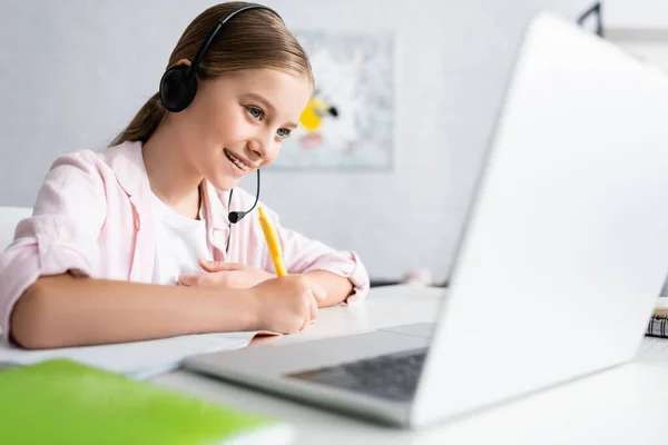 Concentration sélective de l'enfant positif dans l'écriture casque sur ordinateur portable et à l'aide d'un ordinateur portable à la maison — Photo de stock