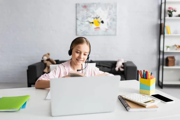 Concentration sélective d'enfant souriant dans le livre de lecture de casque près des gadgets sur la table — Photo de stock