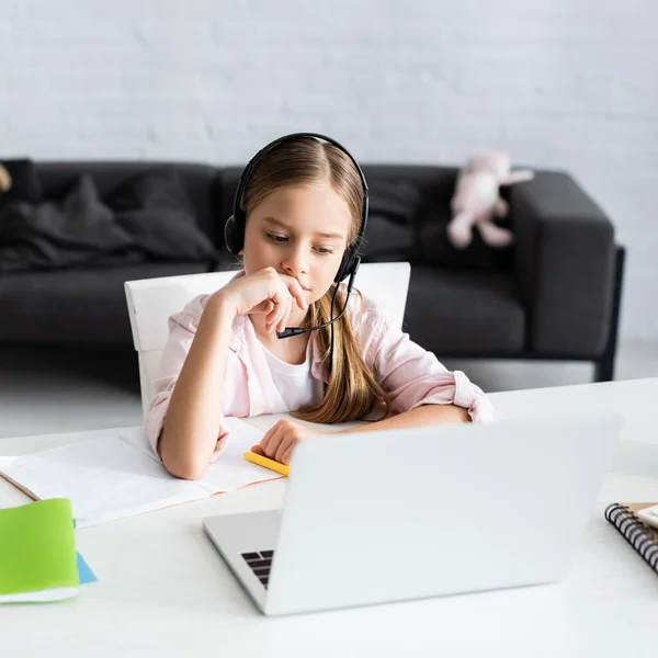 Enfoque selectivo de niño lindo en auriculares sentados cerca de portátil y portátil en la mesa - foto de stock