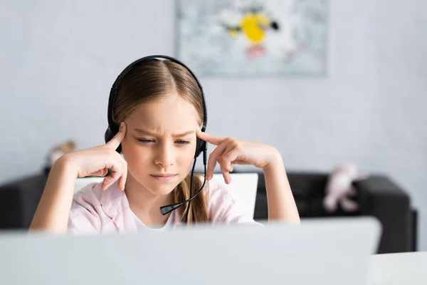 Selective focus of thoughtful kid in headset looking at laptop at home — Stock Photo