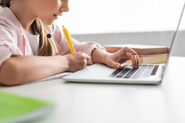 Обрізаний вигляд дитини в гарнітурі, що пише на ноутбуці та використовує ноутбук вдома — стокове фото