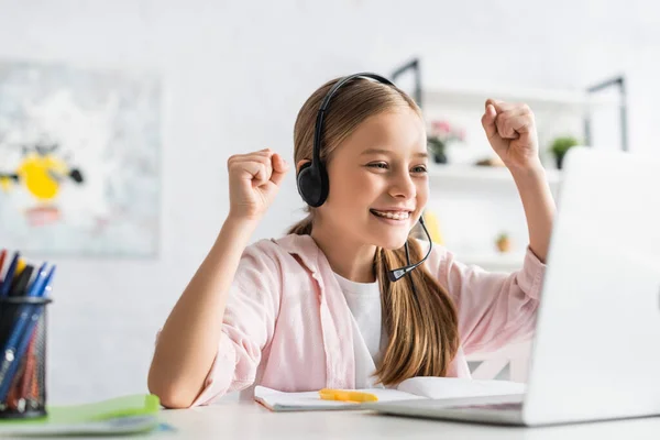 Enfoque selectivo del niño sonriente con auriculares que muestran un gesto de sí durante la educación en línea en el hogar - foto de stock