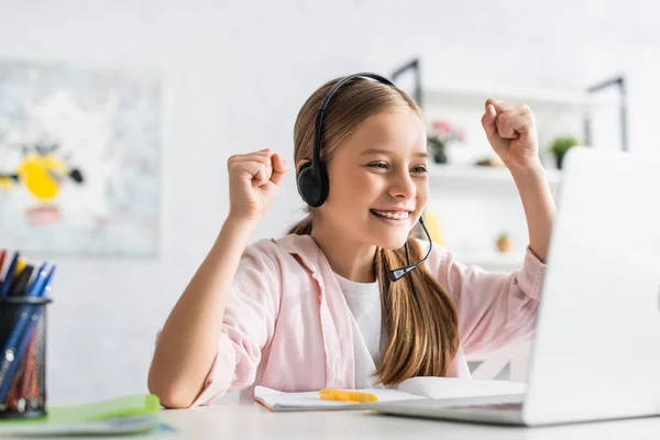 Concentration sélective d'un enfant souriant dans un casque montrant un geste oui lors de l'éducation en ligne à la maison — Photo de stock