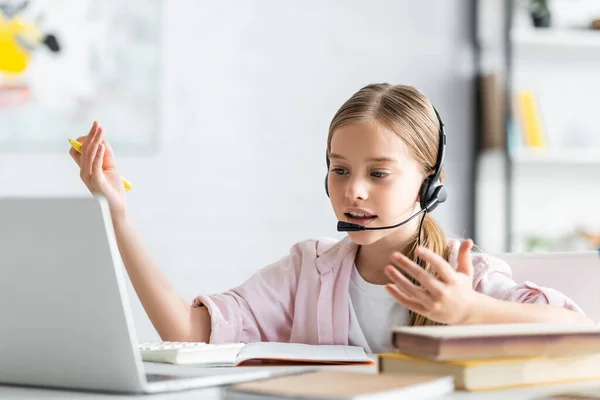 Selective focus of child in headset talking during webinar near books at home — Stock Photo