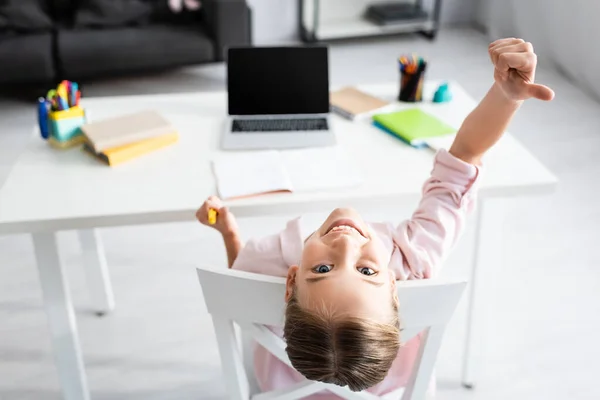 Rückansicht eines lächelnden Kindes, das sich wie eine Geste in der Nähe von Schreibwaren und Laptop zu Hause zeigt — Stockfoto