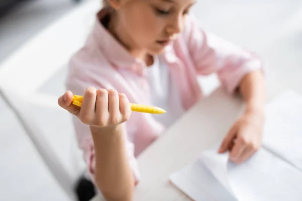 Vista de ángulo alto de niño sosteniendo la pluma y mirando el cuaderno en la mesa - foto de stock