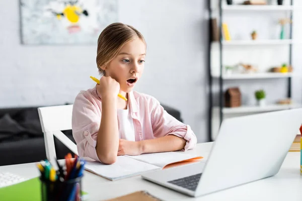 Selective focus of excited child looking at laptop near stationery on table — Stock Photo