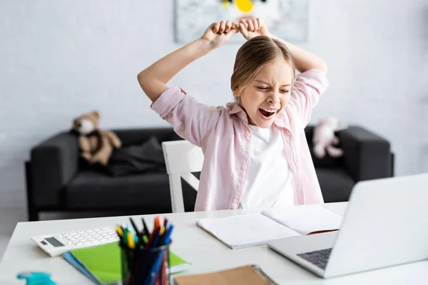 Selective focus of kid yawing and stretching beside laptop and stationery on table — Stock Photo