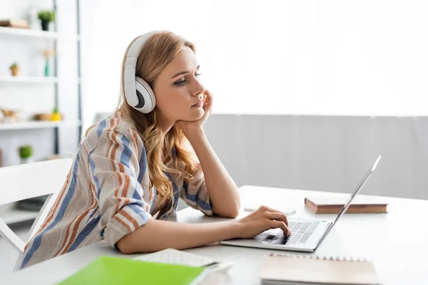 Selective focus of pensive woman working with laptop and headphones — Stock Photo