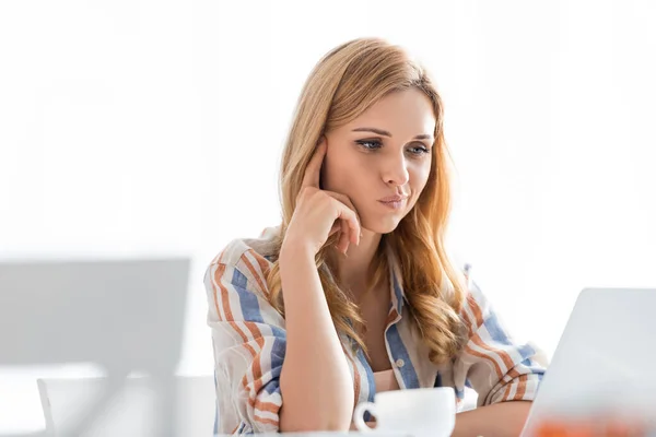 Foco seletivo de mulher pensativa olhando para laptop com xícara de chá — Fotografia de Stock