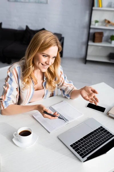 Enfoque selectivo de mujer atractiva sonriendo y haciendo gestos cerca de la computadora portátil y el café - foto de stock