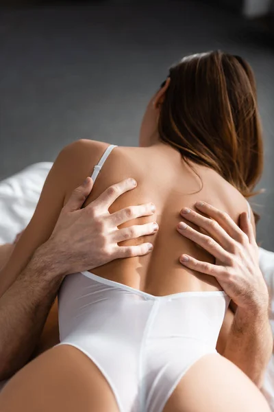 Вид сзади на мужчину, обнимающего сексуальную женщину в белом телесном костюме на кровати — стоковое фото