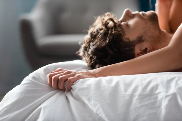 Selektiver Fokus der Frau, die Bettwäsche in der Nähe ihres hübschen Freundes zusammenpresst — Stockfoto