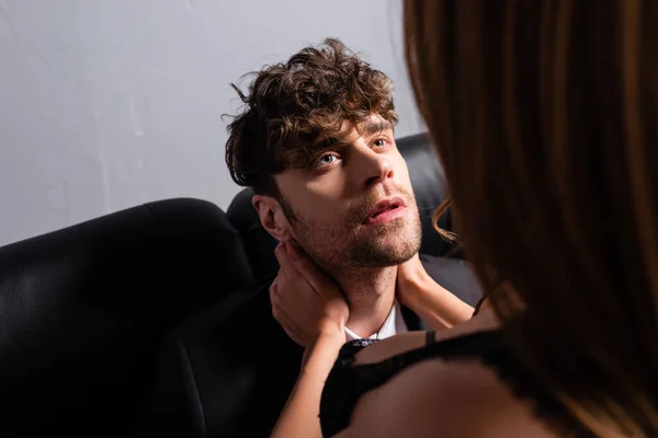 Selective focus of sexy woman in bra embracing neck of handsome boyfriend on couch on grey background — Stock Photo