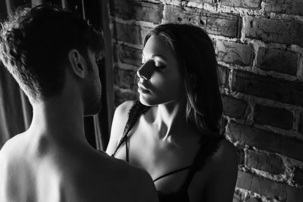 Monochrome image of sexy woman in bra standing near shirtless man and brick wall — Stock Photo