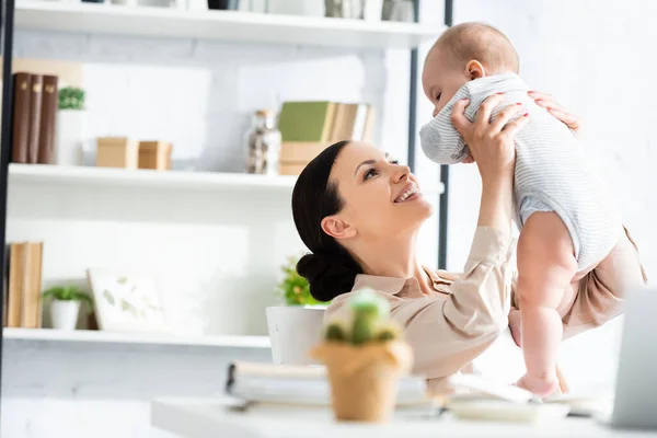 Selektiver Fokus einer glücklichen Mutter, die ihren niedlichen Säugling im Babystrampler im Arm hält — Stockfoto