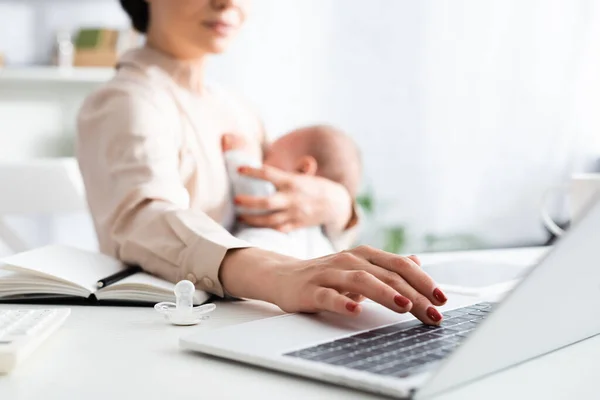 Selective focus of mother breastfeeding infant son while working from home with laptop — Stock Photo