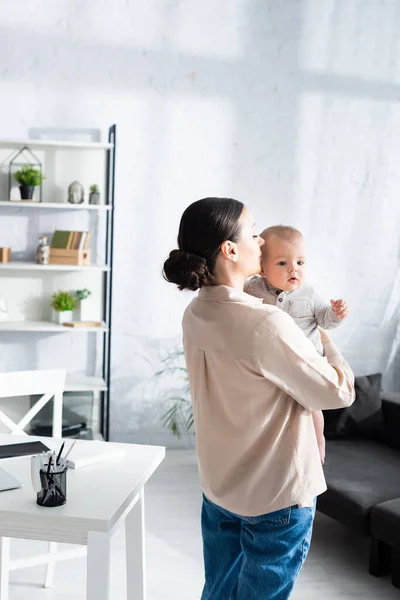 Attractive mother standing and holding in arms cute infant son in baby romper — Stock Photo