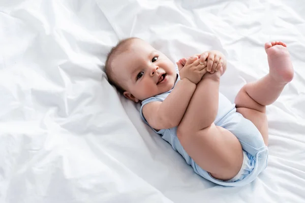 Overhead view of baby boy touching legs while lying on bed — Stock Photo