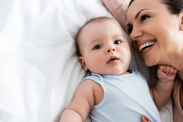 Blick von oben auf eine glückliche Mutter, die in der Nähe eines Säuglings lächelt, während sie auf dem Bett liegt — Stockfoto