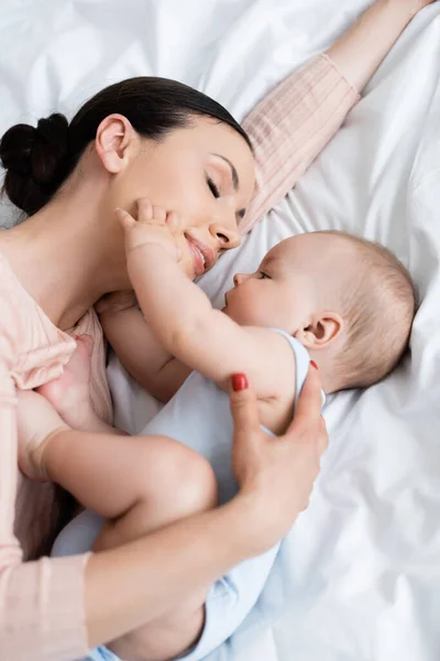 Beautiful mother with closed eyes lying on bed with baby boy — Stock Photo