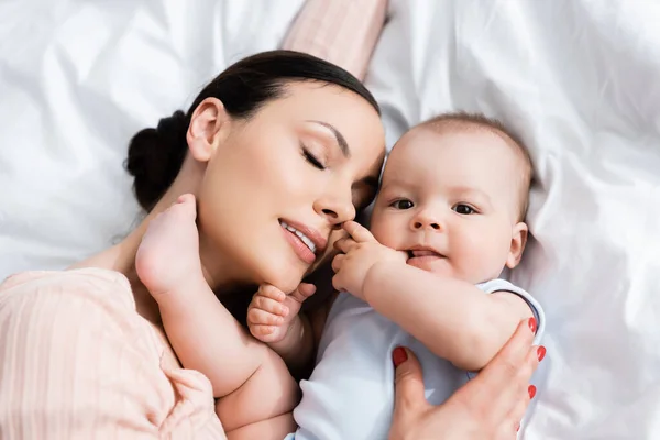 Top view of beautiful mother with closed eyes lying on bed with infant son — Stock Photo