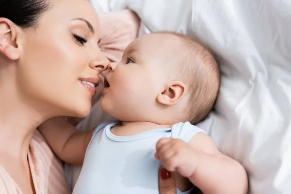 Top view of beautiful mother with closed eyes lying on bed with infant son — Stock Photo