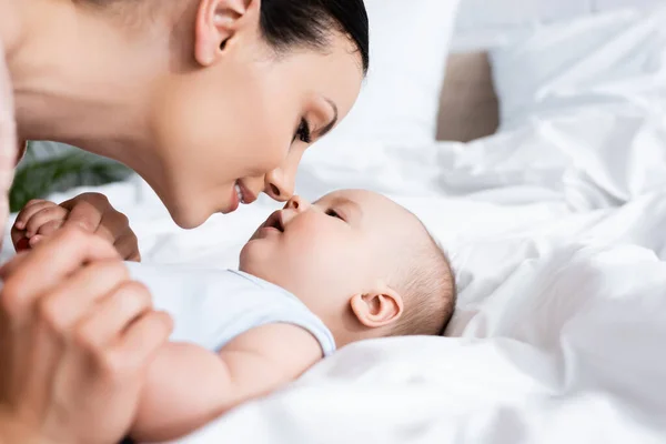 Selective focus of beautiful mother looking at infant son lying on bed — Stock Photo