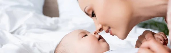 Imagem horizontal da bela mãe olhando para o filho bebê deitado na cama — Fotografia de Stock