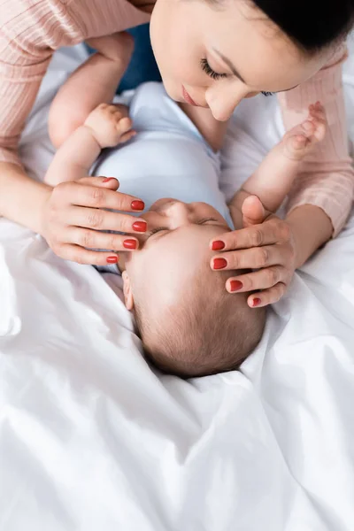 Vista ad alto angolo di madre toccando carino figlio neonato in camera da letto — Foto stock