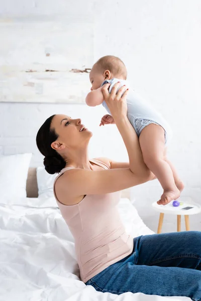 Mãe alegre olhando para o filho bebê bonito no quarto — Fotografia de Stock